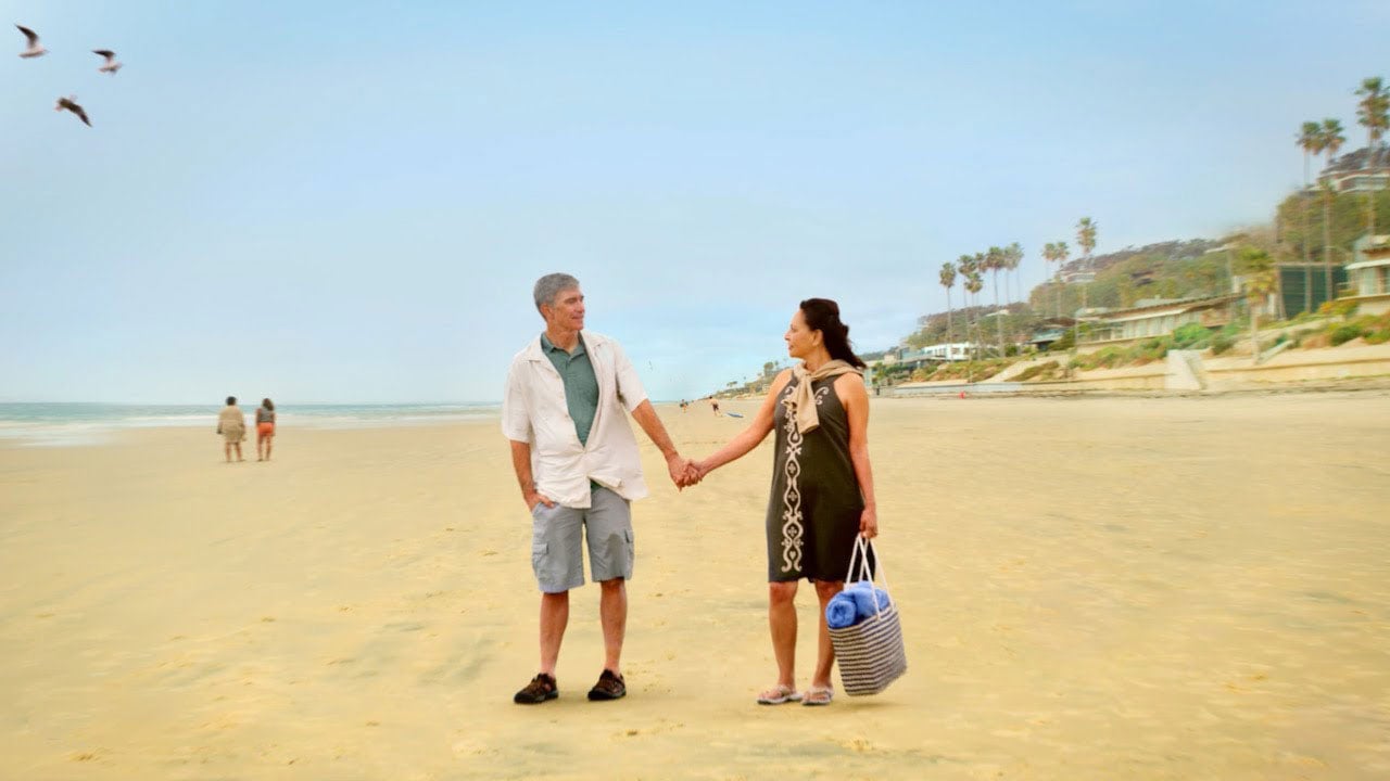 man and woman look at each other holding hands on a beach