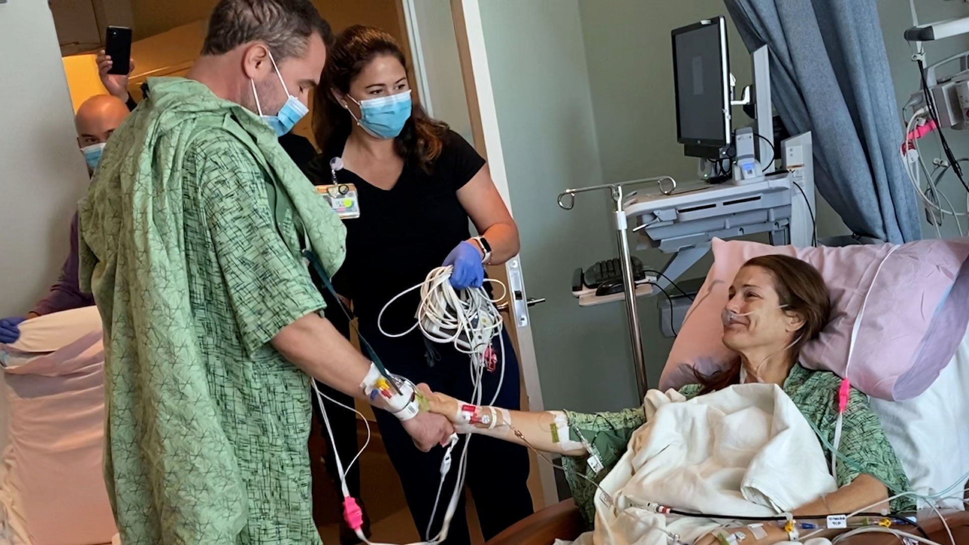 man who donated part of liver (right) shakes hands with patient lying in bed who received it as nurse (middle) watches in hospital room
