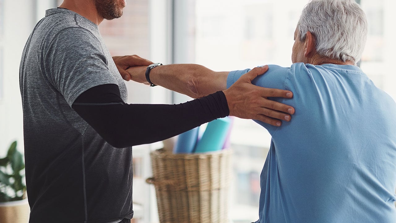 Clinician checking older male patient's arm mobility