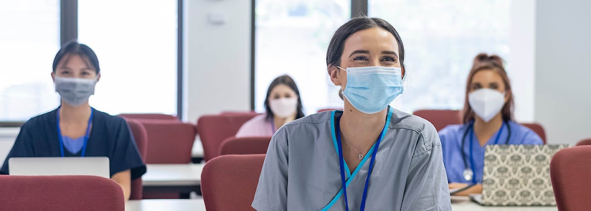 Four women in scrubs take notes in class