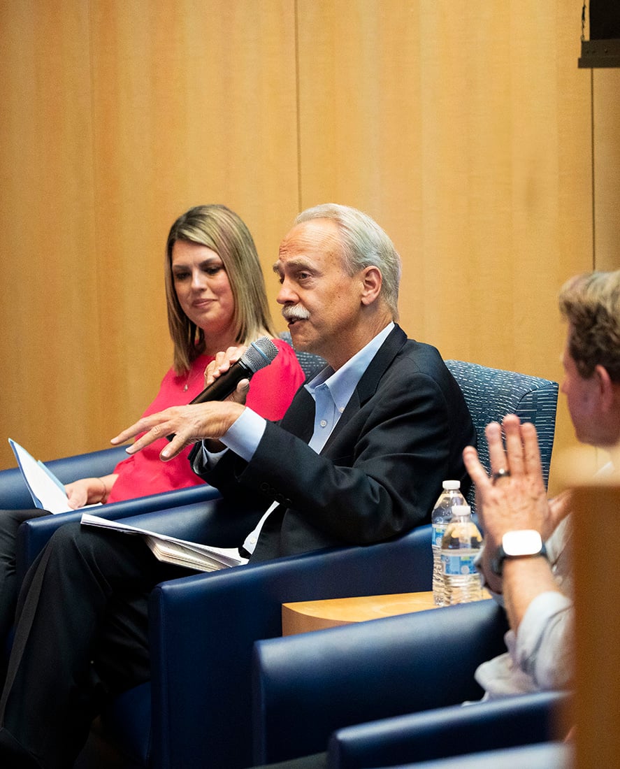 Brubaker and Wormser on stage, seated, Wormser speaking into microphone