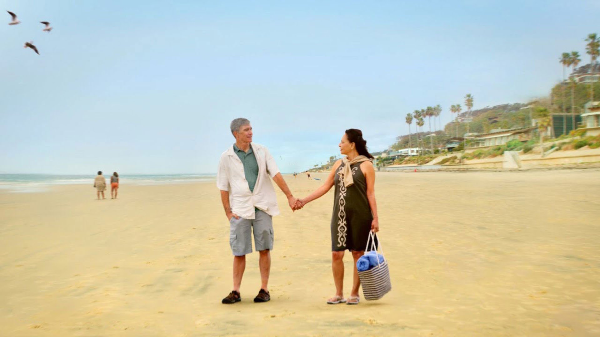 man and woman look at each other holding hands on a beach