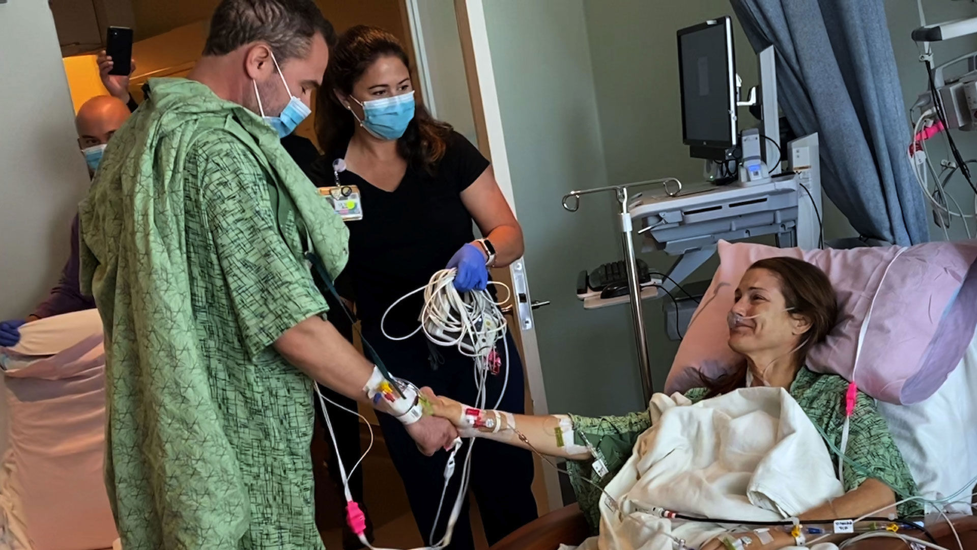 man who donated part of liver (right) shakes hands with patient lying in bed who received it as nurse (middle) watches in hospital room