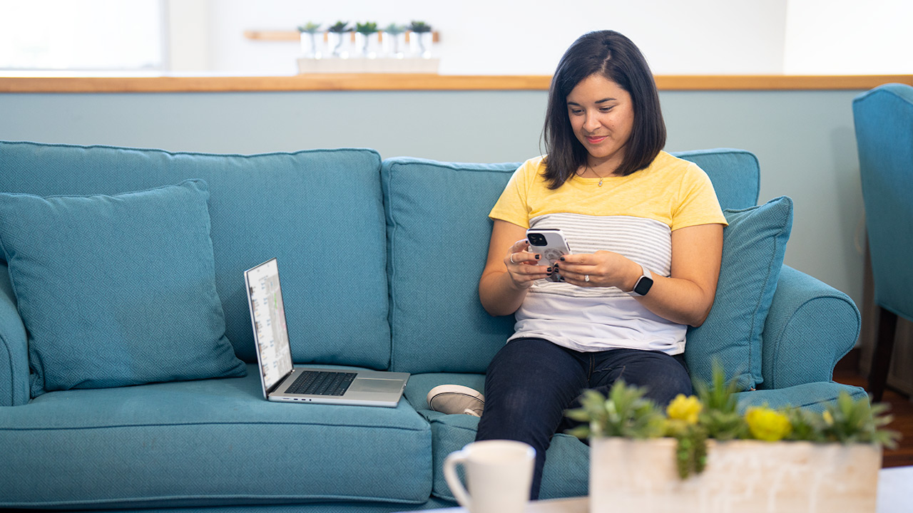 woman sitting on sofa and watching video on cellphone